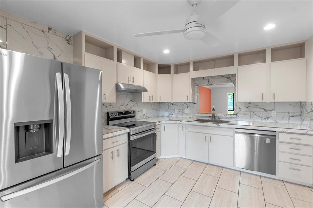 A kitchen features stainless steel appliances, white cabinetry, and marble-patterned countertops and backsplash — 511 LAKESIDE DRIVE UNIT 511, BRADENTON, FL