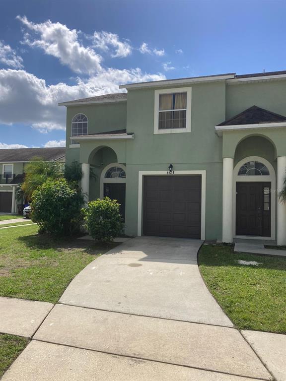A two-story green townhouse features a single-car garage, a concrete driveway, and arched entryways — 4324 PARADISE COVE COURT, KISSIMMEE, FL