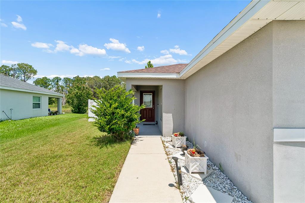 A concrete walkway leads to the front entrance of a single-story house with stucco siding — 6917 GIDEON CIRCLE, ZEPHYRHILLS, FL