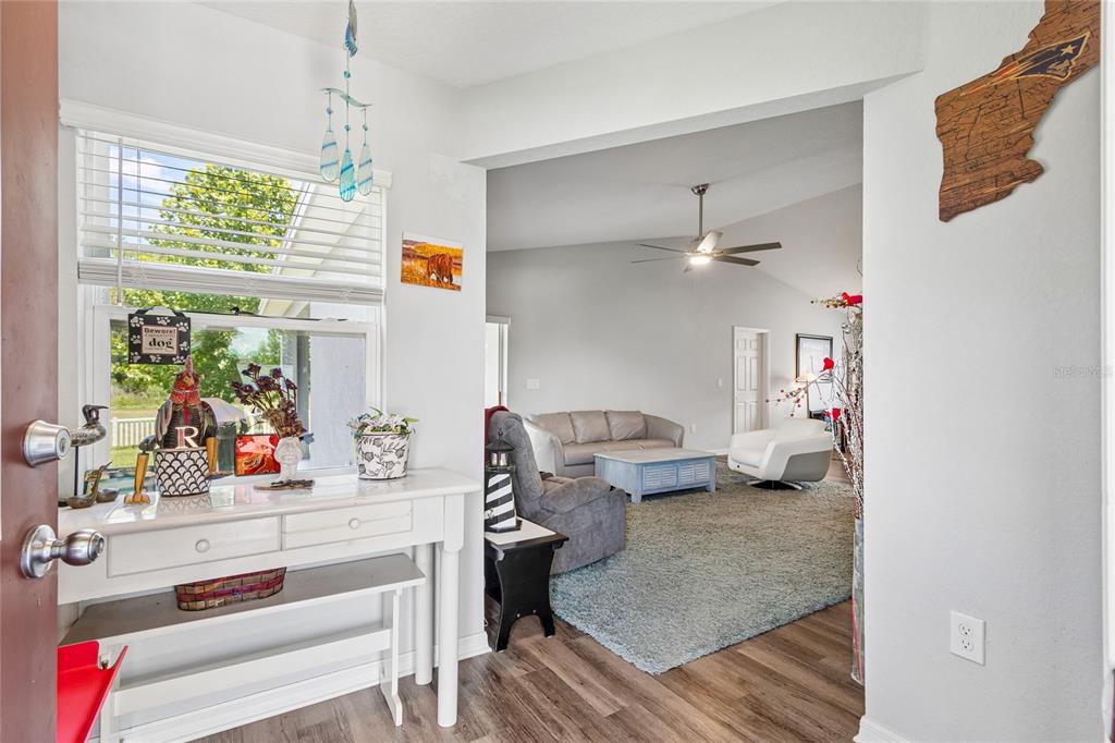 A white entryway console table sits before a window, opening into a carpeted living room — 6917 GIDEON CIRCLE, ZEPHYRHILLS, FL