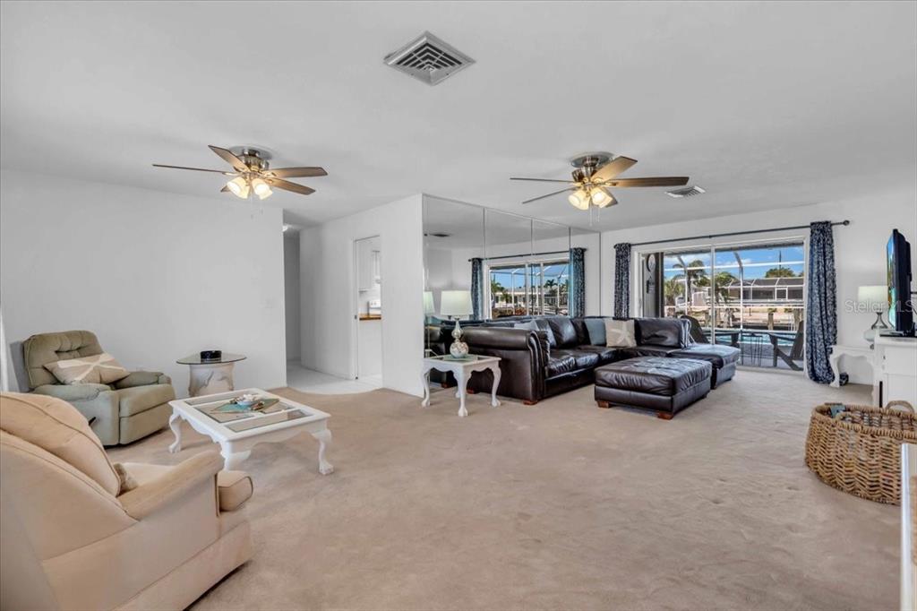 A living room features beige carpeting, a leather sectional, two armchairs, and a mirrored wall — 3816 ROYAL PALM DRIVE, BRADENTON, FL