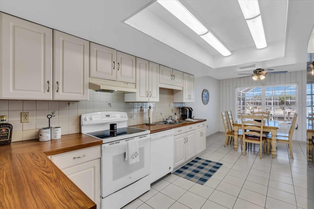 A kitchen with white cabinets, wood countertops, white appliances, and an adjacent dining area — 3816 ROYAL PALM DRIVE, BRADENTON, FL