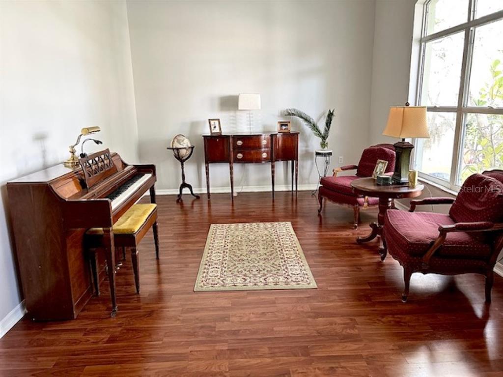 A room with hardwood floors, a piano, a sideboard, and two red armchairs near windows — 1135 BIG SKY DRIVE, WESLEY CHAPEL, FL
