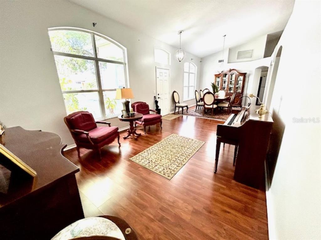 A living and dining area features hardwood floors, a piano, and large arched windows — 1135 BIG SKY DRIVE, WESLEY CHAPEL, FL