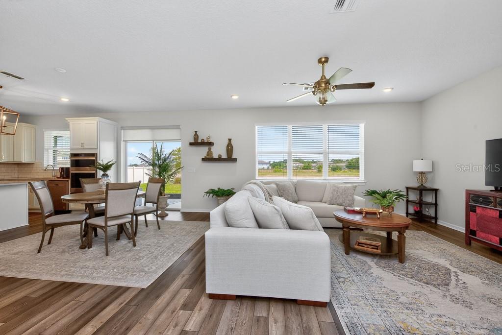 An open-concept living and dining room with wood-look flooring, a ceiling fan, and large windows — 12908 BROOKSIDE MOSS DRIVE, RIVERVIEW, FL