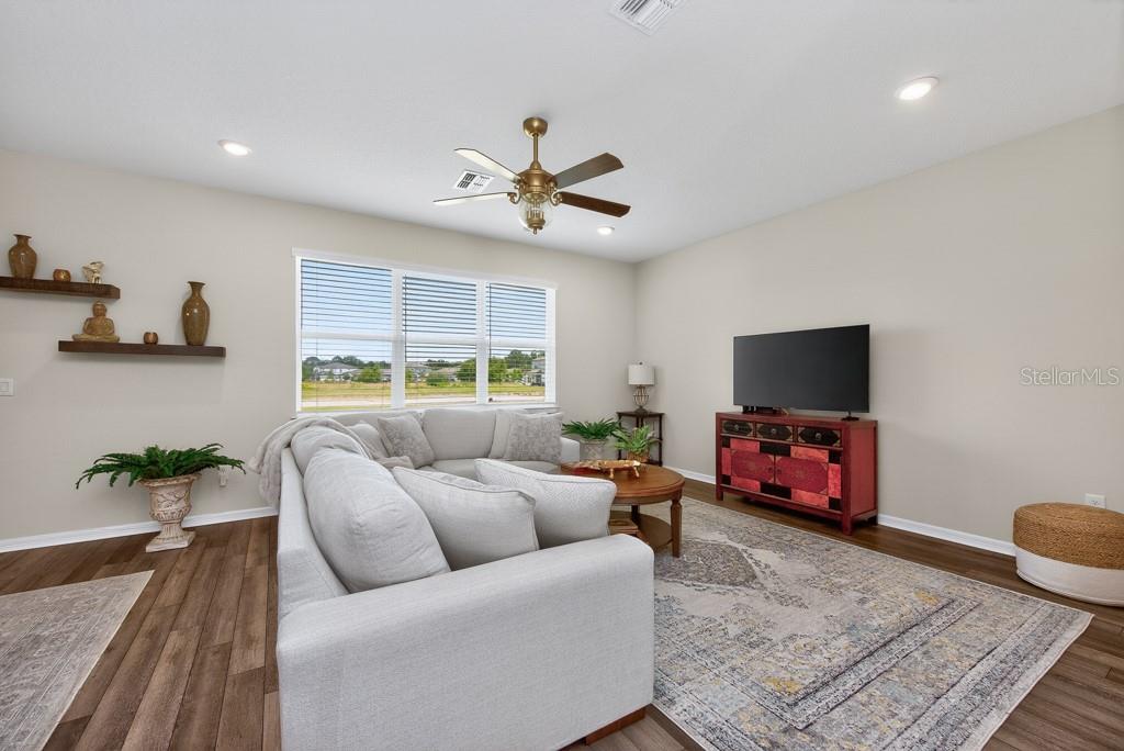 A living room features a sectional sofa, a television on a red cabinet, and wood flooring — 12908 BROOKSIDE MOSS DRIVE, RIVERVIEW, FL