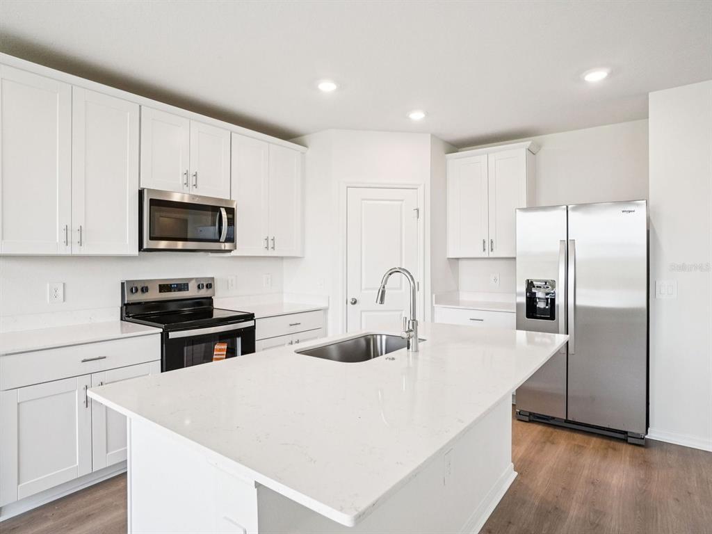 A modern kitchen features white cabinets, stainless steel appliances, and a large quartz island — 3308 ROCKS RIVER ROAD, DAVENPORT, FL