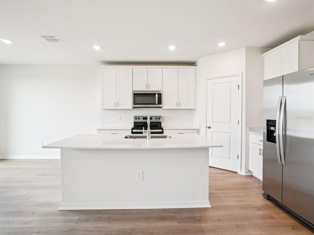 A modern kitchen features white cabinets, a central island with a sink, and stainless appliances — 3308 ROCKS RIVER ROAD, DAVENPORT, FL
