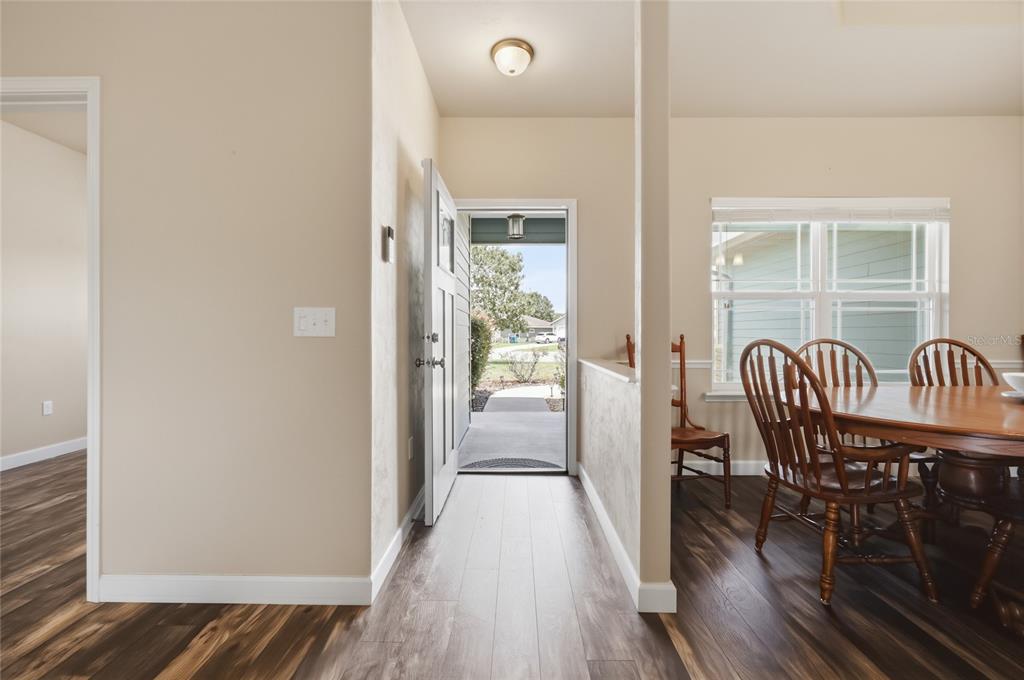 An entryway with wood-look flooring leads to an open front door and a dining area — 22971 NW 6TH LANE, NEWBERRY, FL