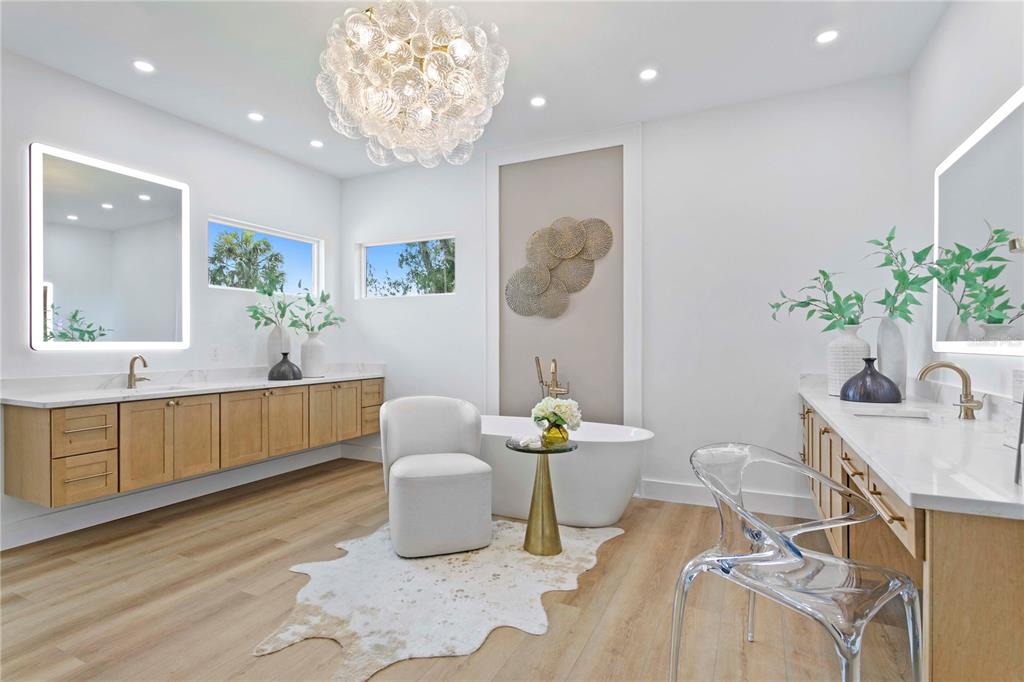 A modern bathroom features a freestanding tub, dual vanities, light wood flooring, and a chandelier — 2202 NEWBERGER ROAD, LUTZ, FL