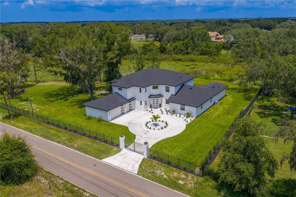An aerial view of a white two-story house with a circular driveway and black roof — 2202 NEWBERGER ROAD, LUTZ, FL