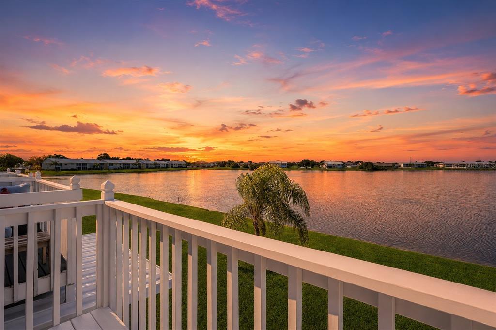 A white wooden balcony railing overlooks a lake at sunset with houses in the distance — 26310 RAMPART BOULEVARD UNIT D504, PUNTA GORDA, FL
