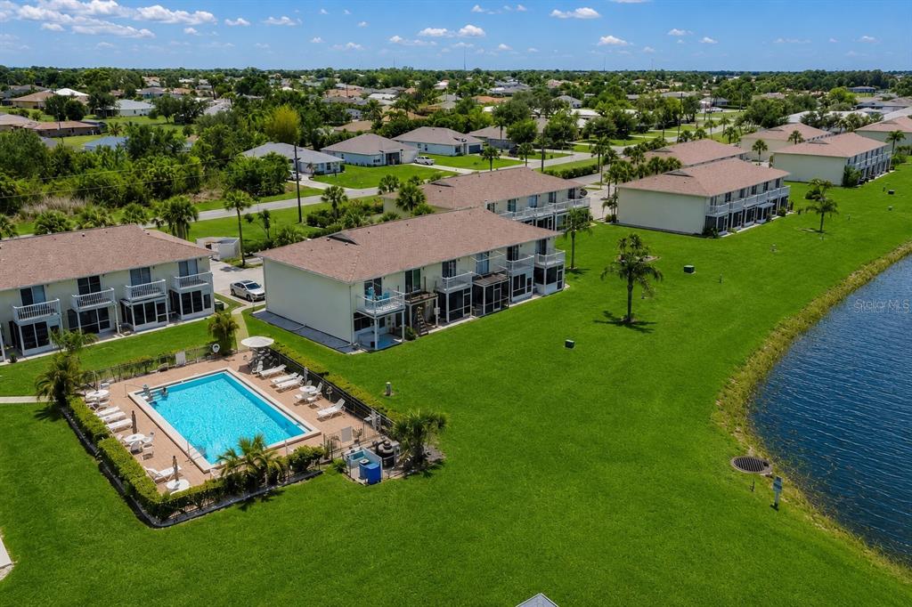 An aerial view of a residential complex with a swimming pool and a nearby pond — 26310 RAMPART BOULEVARD UNIT D504, PUNTA GORDA, FL
