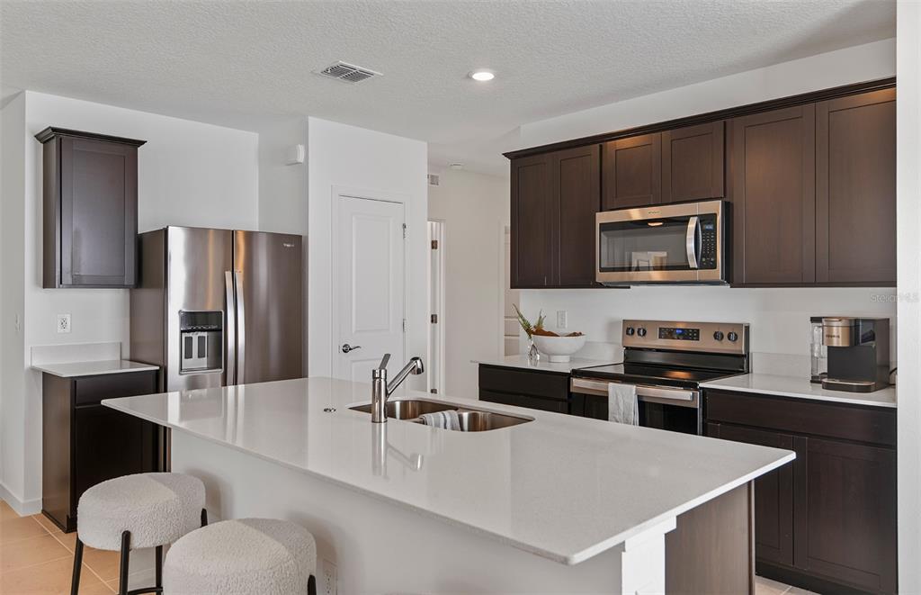 A kitchen features dark wood cabinets, white countertops, a central island, and stainless steel appliances — 5266 CURRANT STREET, LAKELAND, FL