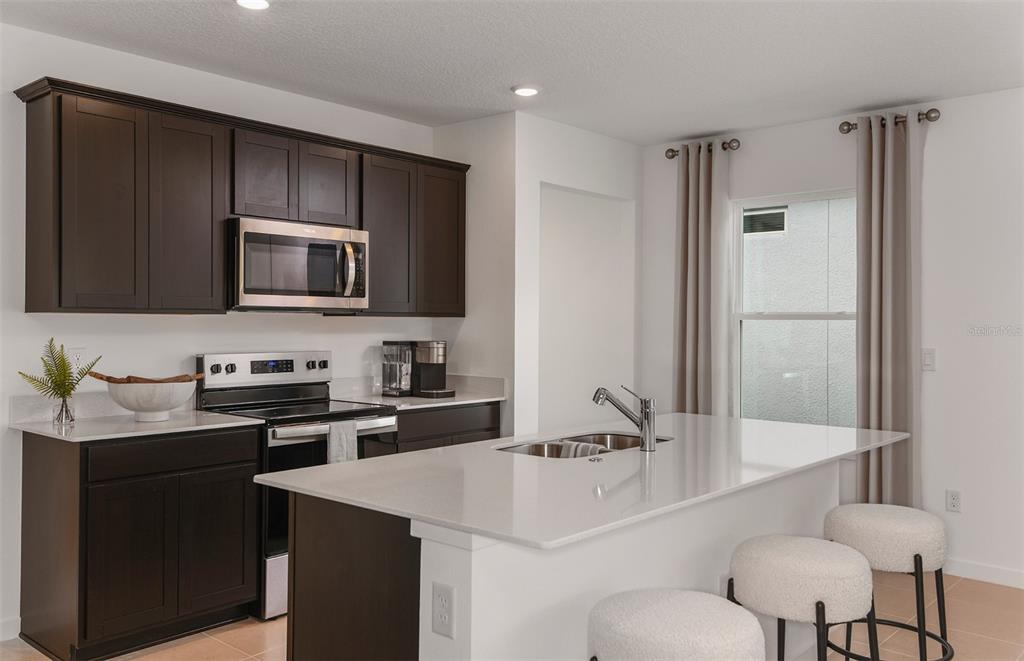 A kitchen features dark wood cabinets, white countertops, a central island, and stainless steel appliances — 5266 CURRANT STREET, LAKELAND, FL