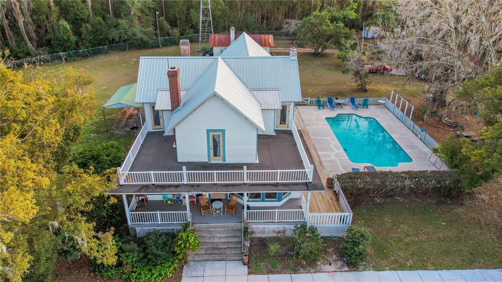 An aerial view of a white farmhouse with a metal roof, wraparound porch, and swimming pool — 9210 COUNTY ROAD 48, YALAHA, FL