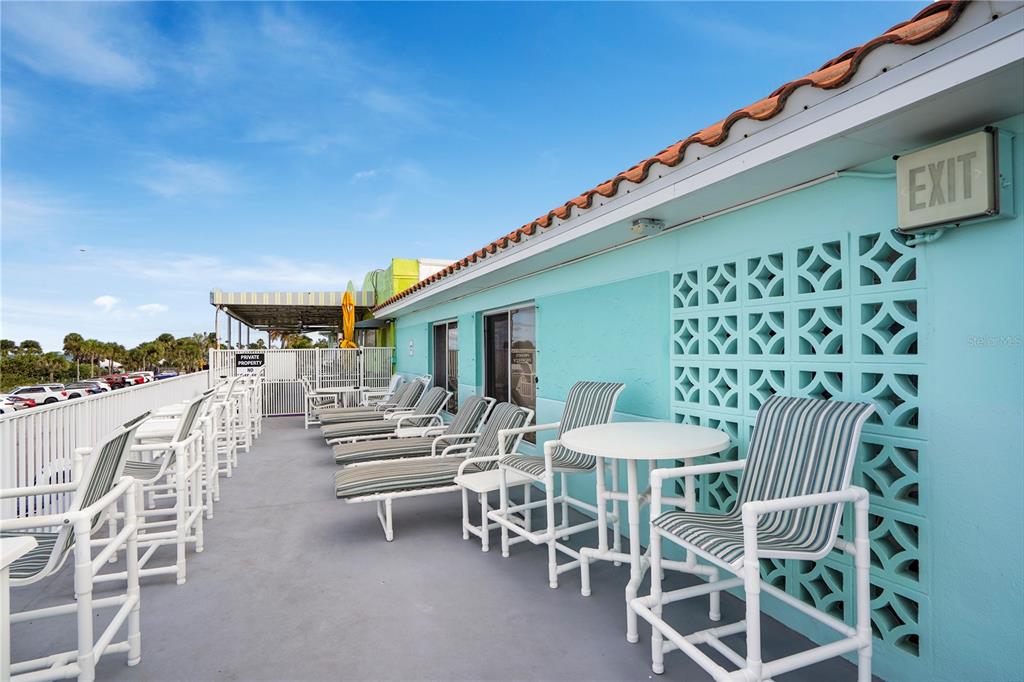 An outdoor patio features lounge chairs and tables against a light blue building exterior — 709 GULF WAY UNIT 19, ST PETE BEACH, FL