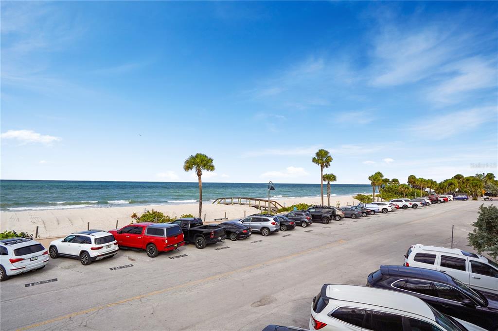 A parking lot sits adjacent to a sandy beach and the ocean under a blue sky — 709 GULF WAY UNIT 19, ST PETE BEACH, FL