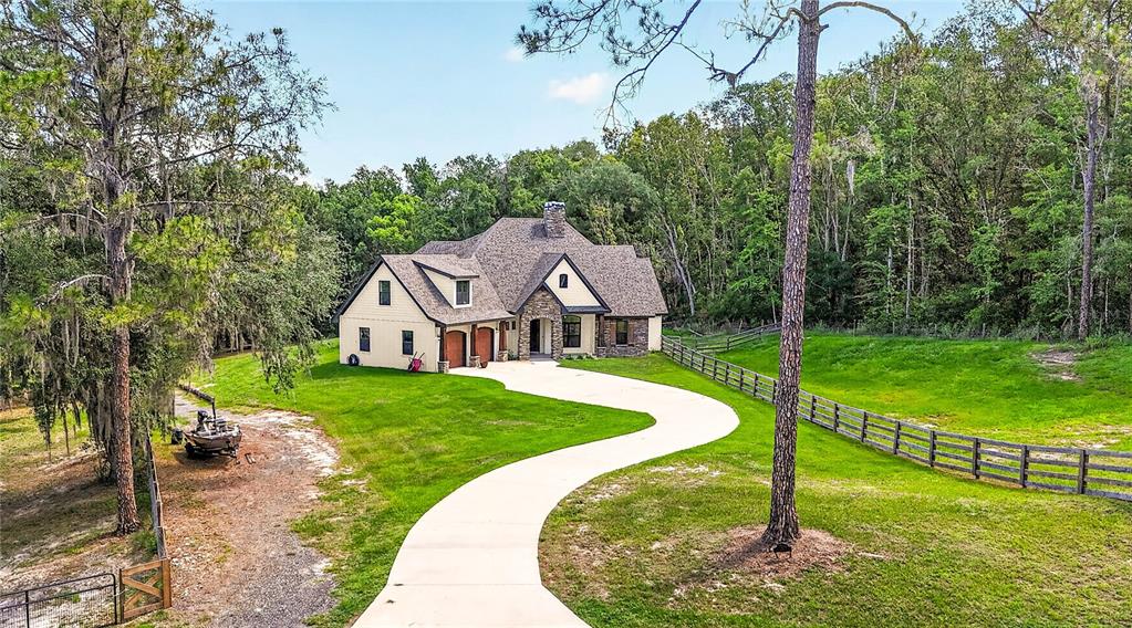 An aerial view shows a multi-story house with a stone facade and a curved driveway — 17265 MEADOW BLUFF VIEW, DADE CITY, FL