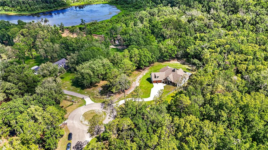 An aerial view shows a house with a driveway surrounded by dense forest and water — 17265 MEADOW BLUFF VIEW, DADE CITY, FL