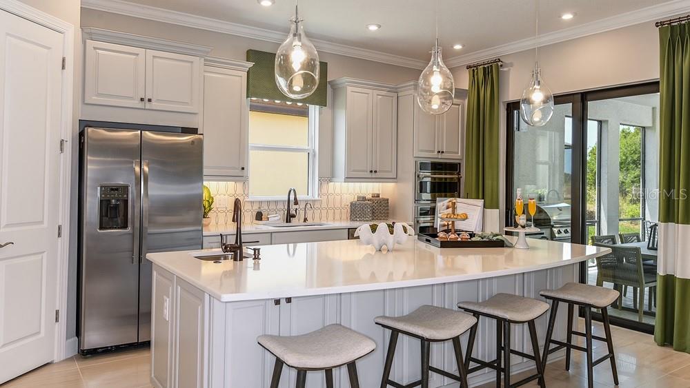 A modern kitchen features white cabinetry, a large center island with bar seating, and pendant lighting — 29668 IMPERATI BOULEVARD, WESLEY CHAPEL, FL