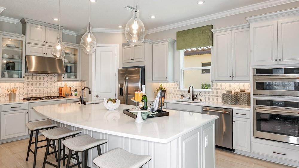 A modern kitchen features white cabinetry, a large quartz island, stainless steel appliances, and pendant lighting — 29668 IMPERATI BOULEVARD, WESLEY CHAPEL, FL