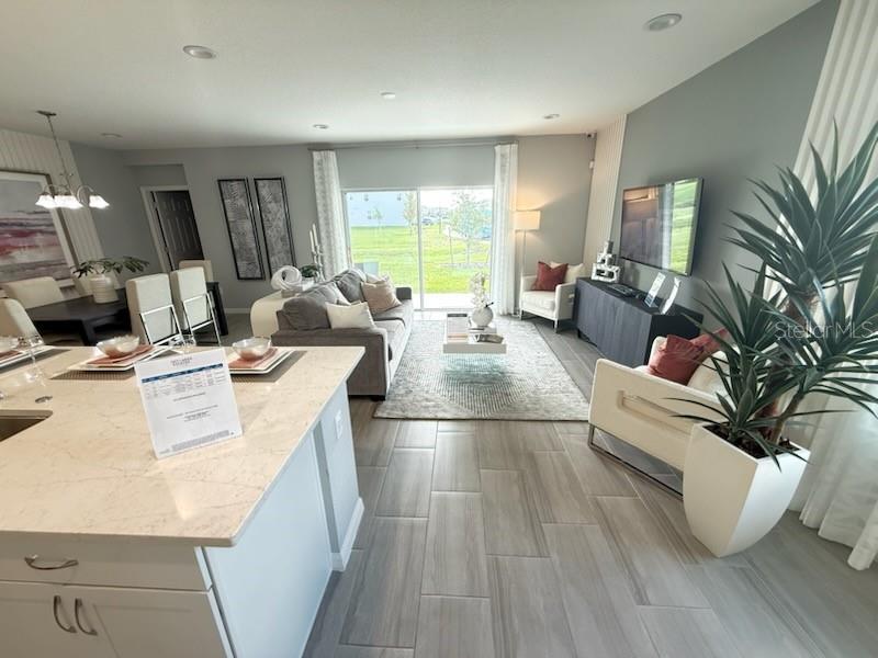An open-concept living room and kitchen area with tile flooring, neutral decor, and sliding glass doors — 2677 STARRY POINT, ST CLOUD, FL