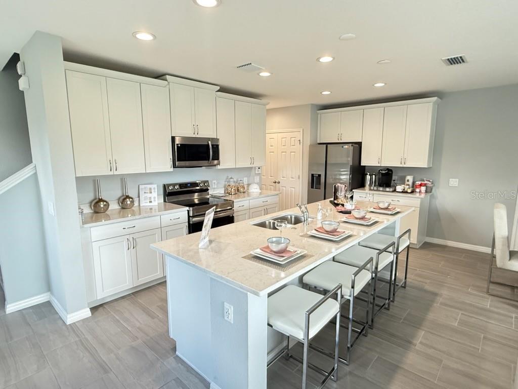 A modern kitchen features white cabinetry, stainless steel appliances, and a large quartz-topped island — 2677 STARRY POINT, ST CLOUD, FL