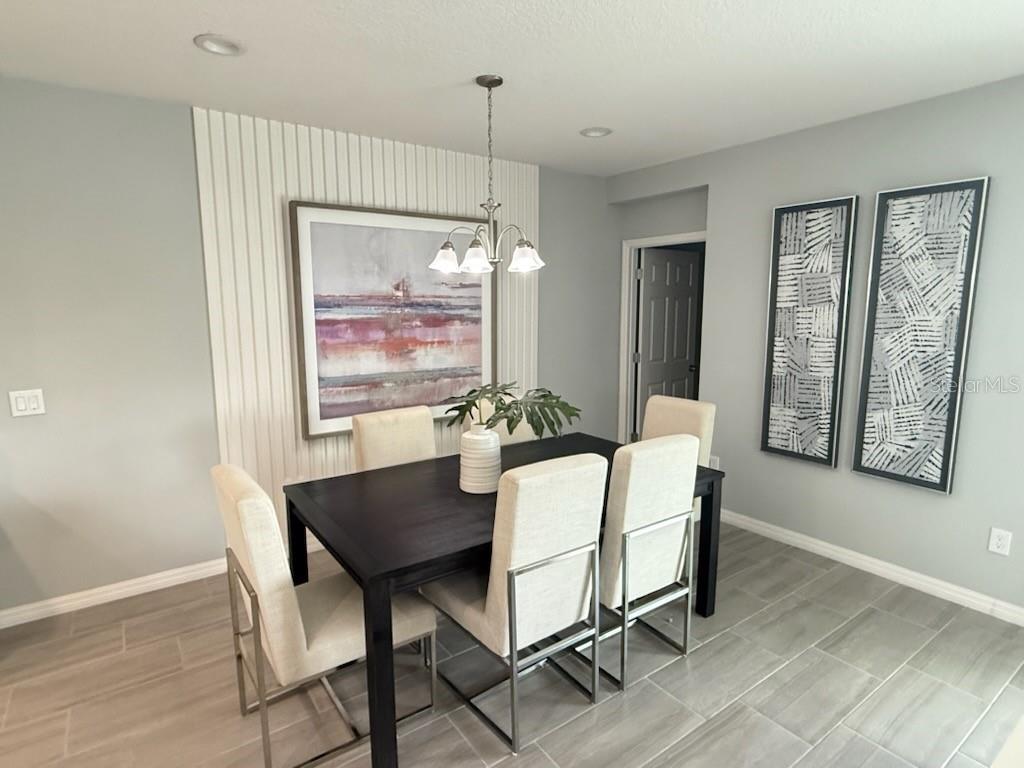 A dining room features a dark table, upholstered chairs, vertical wall paneling, and abstract artwork — 2677 STARRY POINT, ST CLOUD, FL