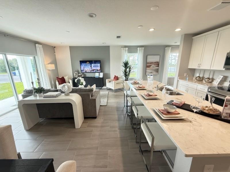 An open-concept living room and kitchen featuring tile floors, white cabinetry, and a large island — 2677 STARRY POINT, ST CLOUD, FL