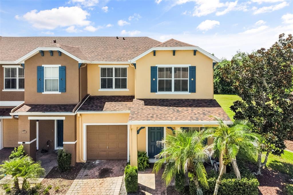 An exterior view of a two-story townhouse with a tan facade, garage, and blue shutters — 16424 CEDAR CREST DRIVE, ORLANDO, FL