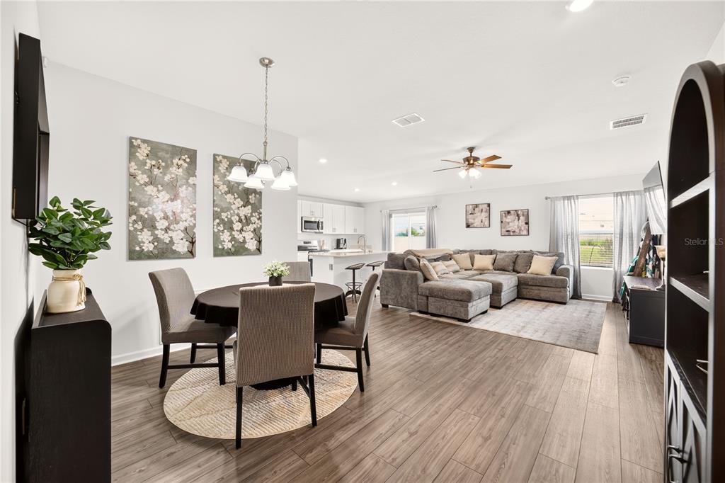 An open-concept living and dining area features wood-look flooring, a sectional sofa, and kitchen — 4745 SW 83RD LOOP, OCALA, FL
