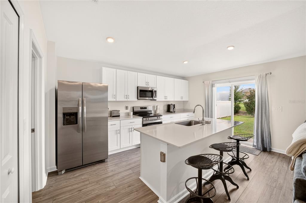 A modern kitchen features white cabinets, stainless steel appliances, a center island, and wood flooring — 4745 SW 83RD LOOP, OCALA, FL