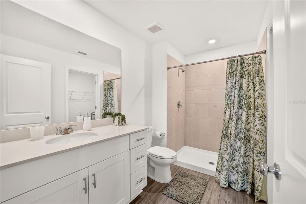 A bathroom features a white vanity, a walk-in shower with beige tile, and wood-look flooring — 4745 SW 83RD LOOP, OCALA, FL