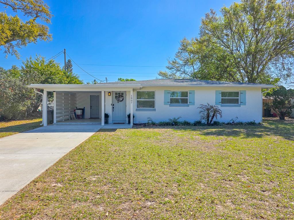 A single-story white house with a carport and blue shutters sits on a grassy lot — 1807 GOLFVIEW BOULEVARD, SOUTH DAYTONA, FL