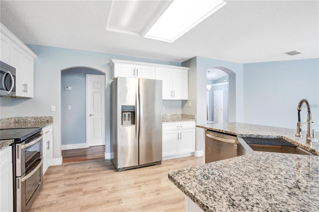 A kitchen features white cabinets, granite countertops, stainless steel appliances, and light wood flooring — 14203 VISTA DEL LAGO BOULEVARD, CLERMONT, FL