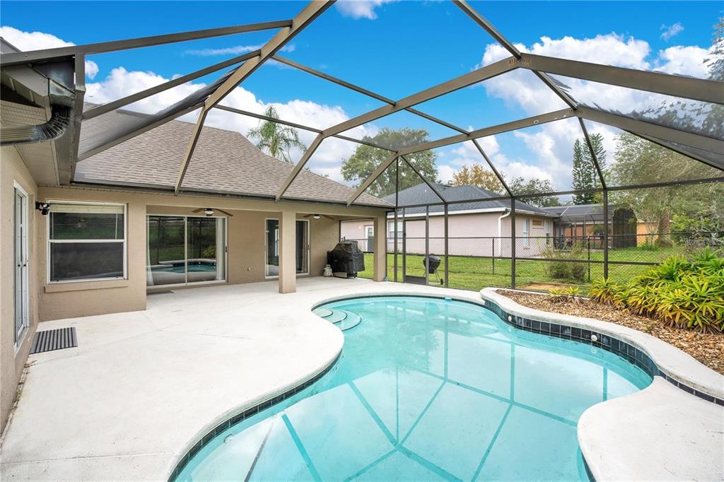 A screened-in patio features a kidney-shaped swimming pool and a concrete deck — 14203 VISTA DEL LAGO BOULEVARD, CLERMONT, FL