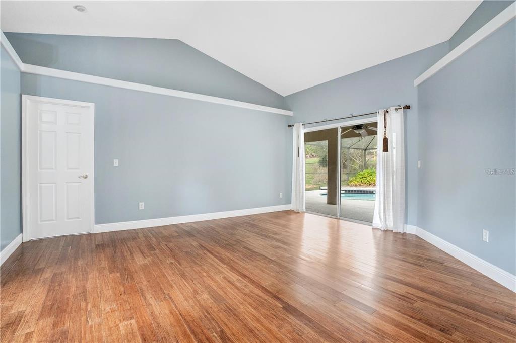 An empty room with light blue walls, vaulted ceilings, hardwood floors, and sliding glass doors — 14203 VISTA DEL LAGO BOULEVARD, CLERMONT, FL