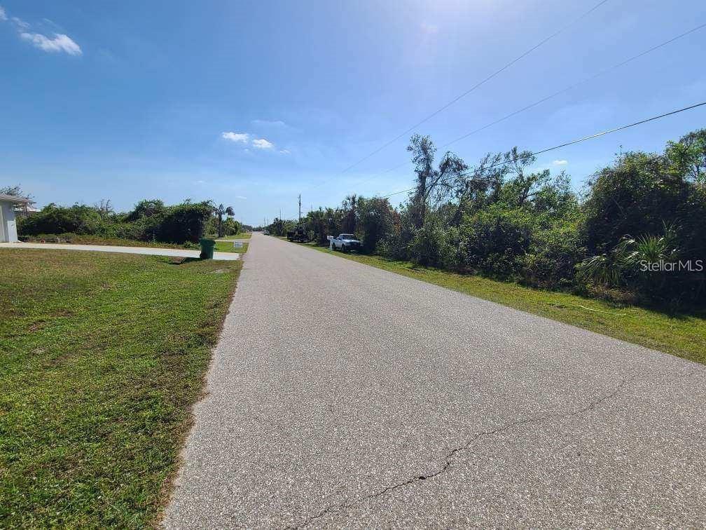 A paved road stretches into the distance between grassy lots and dense vegetation — 6441 ROBERTA DRIVE, ENGLEWOOD, FL