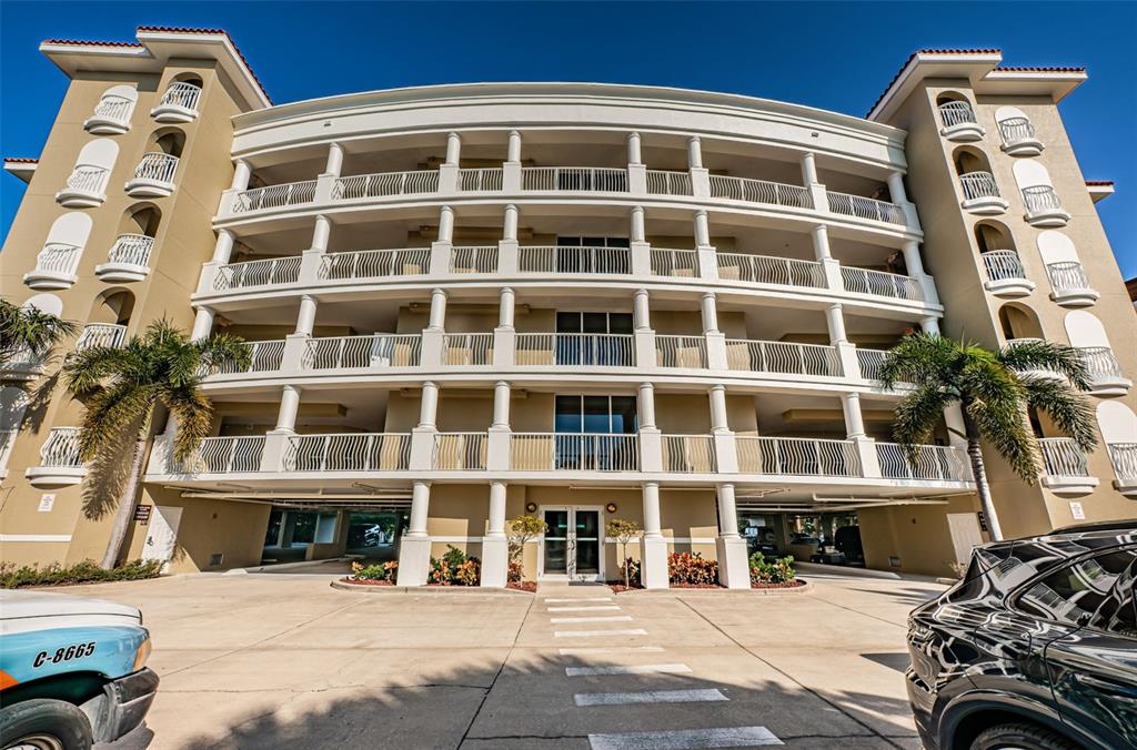The exterior of a multi-story apartment building features white balconies, columns, and a ground-level entrance — 3805 GULF BOULEVARD UNIT 504, ST PETE BEACH, FL