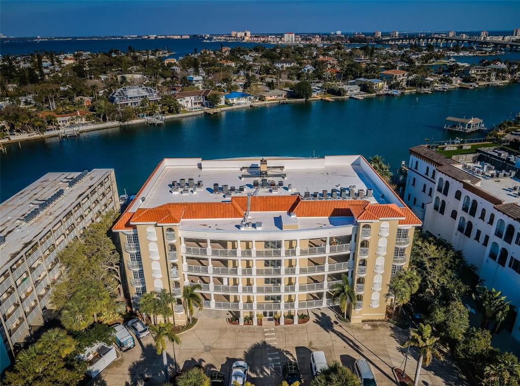 An aerial view of a multi-story apartment building with a red tile roof near water — 3805 GULF BOULEVARD UNIT 504, ST PETE BEACH, FL