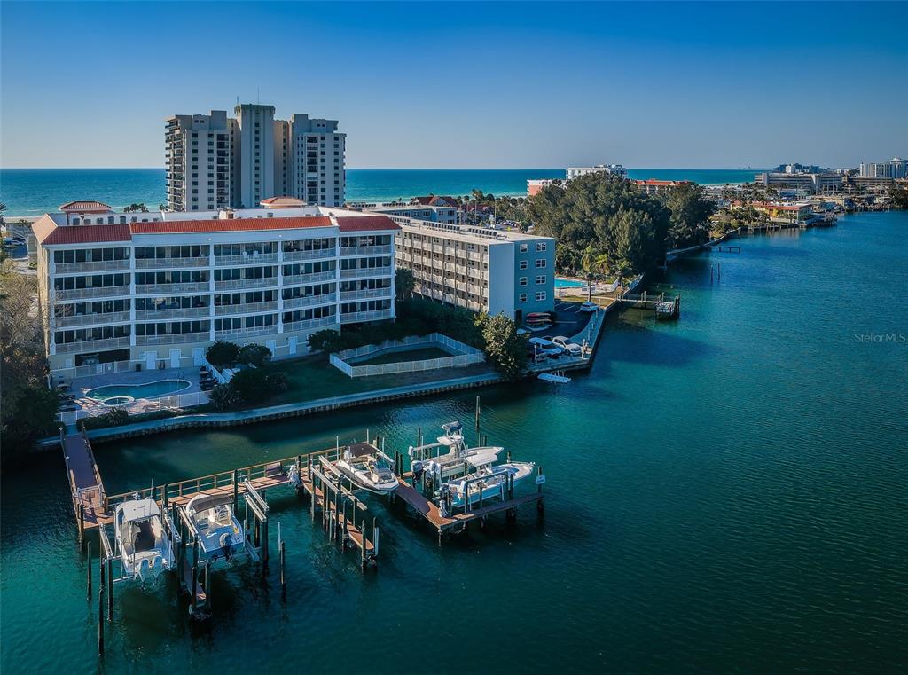 An aerial view shows a waterfront apartment complex with boat docks and a swimming pool — 3805 GULF BOULEVARD UNIT 504, ST PETE BEACH, FL