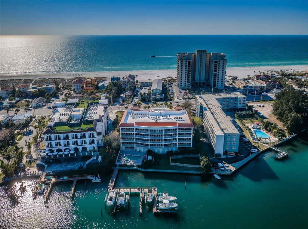 An aerial view shows waterfront condominiums, a boat dock, and a beach along the ocean — 3805 GULF BOULEVARD UNIT 504, ST PETE BEACH, FL