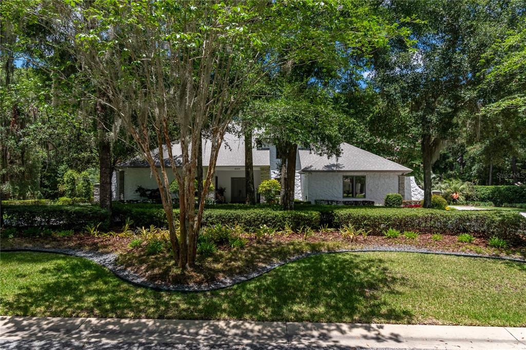 A white house with a gray roof sits behind a manicured hedge and large trees — 5004 SE 5TH AVENUE, OCALA, FL
