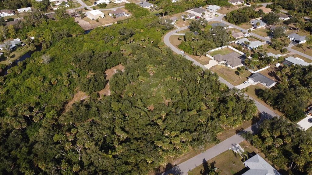 An aerial view shows a wooded, undeveloped lot surrounded by residential houses and streets — ALFA TERRACE, NORTH PORT, FL