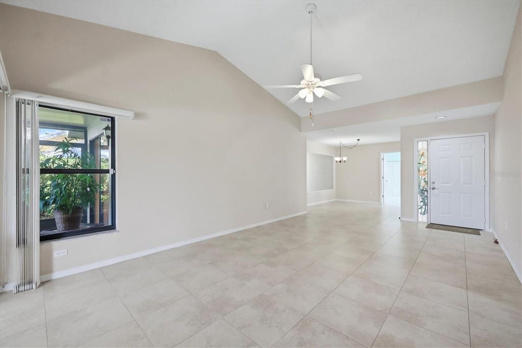 An empty living room with vaulted ceilings, tile flooring, a ceiling fan, and a front door — 214 SOUTHAMPTON DRIVE UNIT 327, VENICE, FL