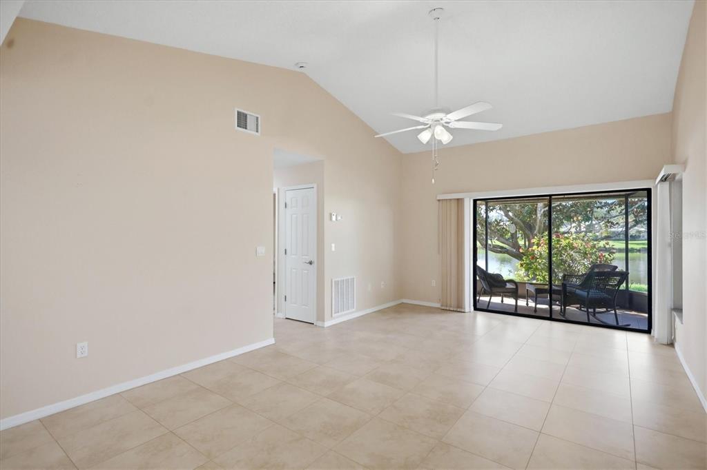 An empty living room with vaulted ceilings, tile floors, and a sliding door to a patio — 214 SOUTHAMPTON DRIVE UNIT 327, VENICE, FL