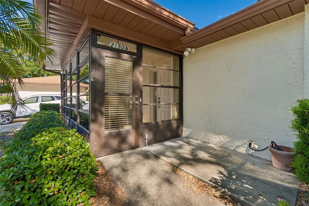 An exterior view of a home entrance featuring a screened-in porch and a concrete walkway — 2150 SHELLY DRIVE UNIT B, PALM HARBOR, FL