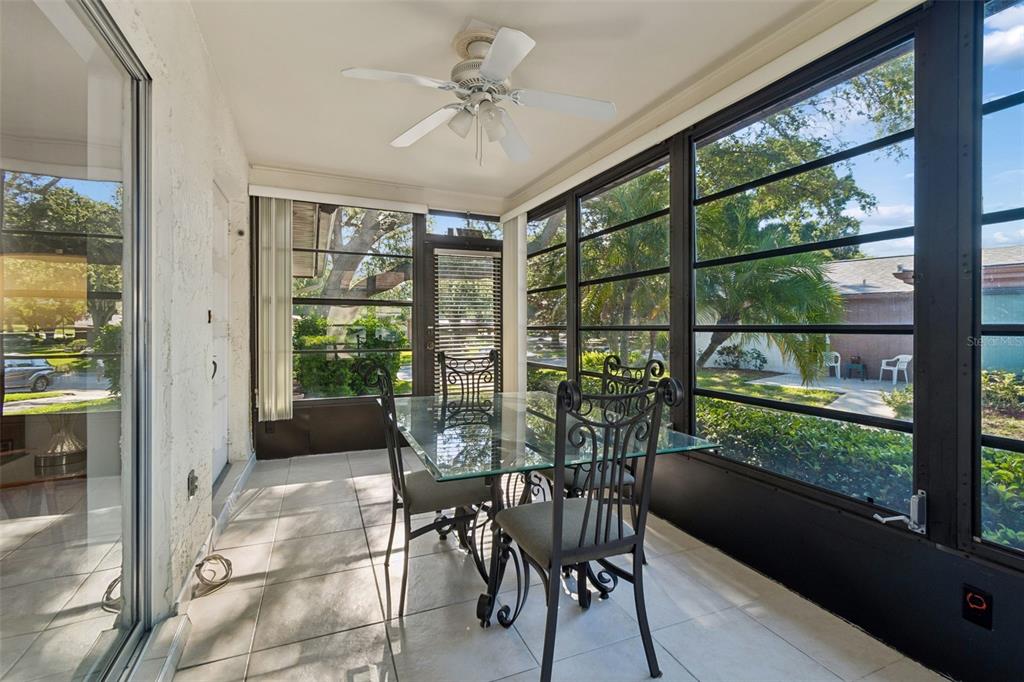 A sunroom features a glass-top dining table, tile flooring, a ceiling fan, and large windows — 2150 SHELLY DRIVE UNIT B, PALM HARBOR, FL
