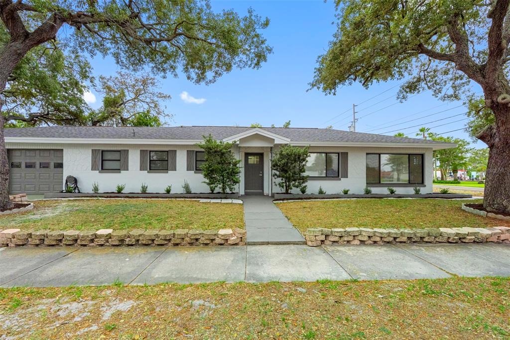A single-story white house with a gray garage door and a stone retaining wall — 1005 APACHE TRAIL, CLEARWATER, FL